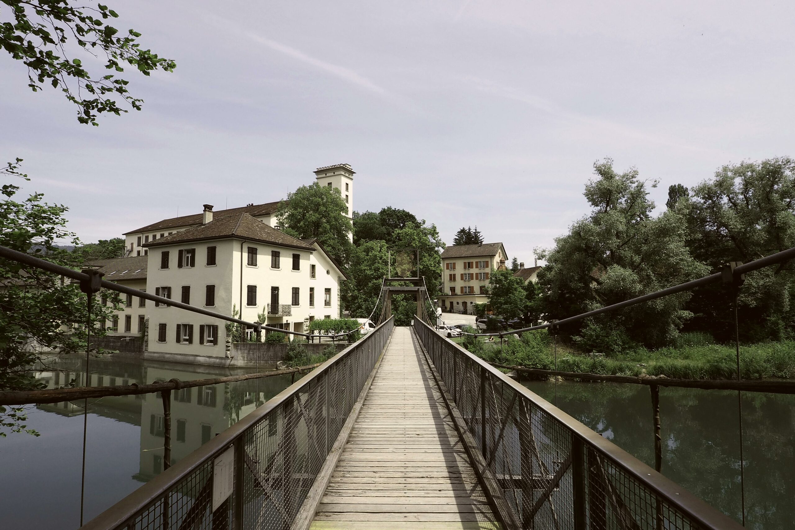 Accueil Charming footbridge leading to historical buildings by a serene river in Wettingen, Switzerland.